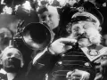 Un uomo con baffi e barba folta suona una tromba, circondato da volti sorridenti. Un'atmosfera da kammerspiel, un dramma intimo e intenso.