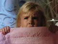 Bambina spaventata si nasconde sotto una coperta rosa, gli occhi sgranati in un'espressione di puro horror psicologico.