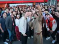 Un gruppo di persone sorride e fa un selfie a Hollywood, America. Alcuni tengono microfoni, creando un'atmosfera di festa.