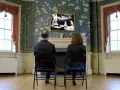 Coppia seduta di spalle, guarda un quadro con una scena di giardino, "Roundhay Garden Scene", su una parete fiorita.