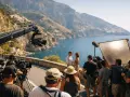 Una troupe cinematografica cattura una scena romantica con una coppia, tra montagne e mare, un'immagine che evoca la magia della hollywood industria cinematografica.