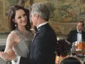Il cast di Revenge balla elegantemente. Una donna con un abito grigio e collane di perle, un uomo in smoking.