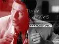 Primo piano di un uomo con un completo chiaro, con un effetto grafico che ricorda il velluto blu trama. Sopra, il logo "Twin Peaks".