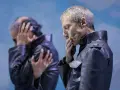 Kjell Brutscheidt, con le mani sul volto, esprime angoscia. L'altro uomo, sfocato, si copre le orecchie.