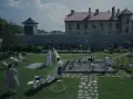 Scena da film strani: bambini giocano in piscina, adulti sorvegliano, mentre sullo sfondo incombono torri di guardia e un edificio imponente.