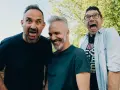 Tre uomini con espressioni esagerate, come in un film comico del cinema muto, ridono e fanno smorfie all'aperto.
