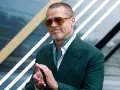 Brad Pitt, icona del cinema hollywoodiano, con occhiali da sole e completo verde, applaude con un sorriso.