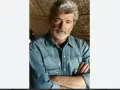 George Lucas, uno dei registi importanti, con barba grigia e camicia di jeans, braccia conserte.