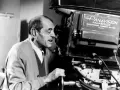 Un regista spagnolo, con un maglione grigio, guarda attraverso l'obiettivo di una cinepresa Panavision.