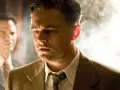 Uomo con cerotto sulla fronte, sguardo intenso, un altro uomo sfocato sullo sfondo. Sembra l'inizio di un colpo di scena.