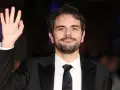 Valerio Vestoso saluta con la mano, sorridendo con un abito elegante.