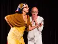 Due attori in scena, una donna con foulard e grembiule giallo, un uomo con le mani sul volto. Una scena di commedia drammatica.
