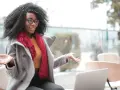 Donna con capelli ricci e occhiali spiega come fare un trailer, gesticolando con le mani davanti a un laptop.