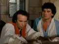 Due uomini in abiti d'epoca, uno scrive con una penna d'oca, in una scena che promette un film comico.