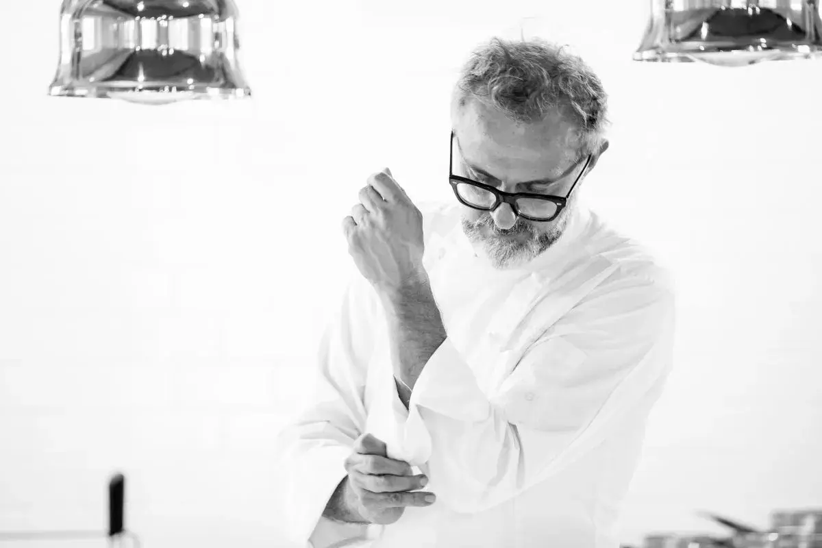 Julian works, aggiustandosi il polsino della giacca da chef. La sua espressione concentrata suggerisce la dedizione al suo mestiere.