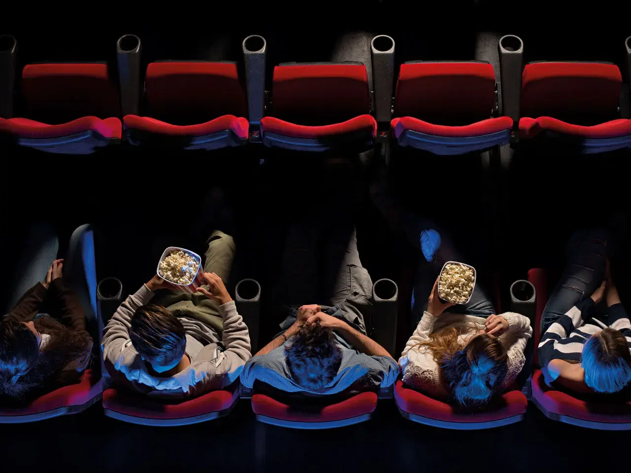 Persone sedute in un cinema, gustando popcorn, pronte per un film di Hollywood.