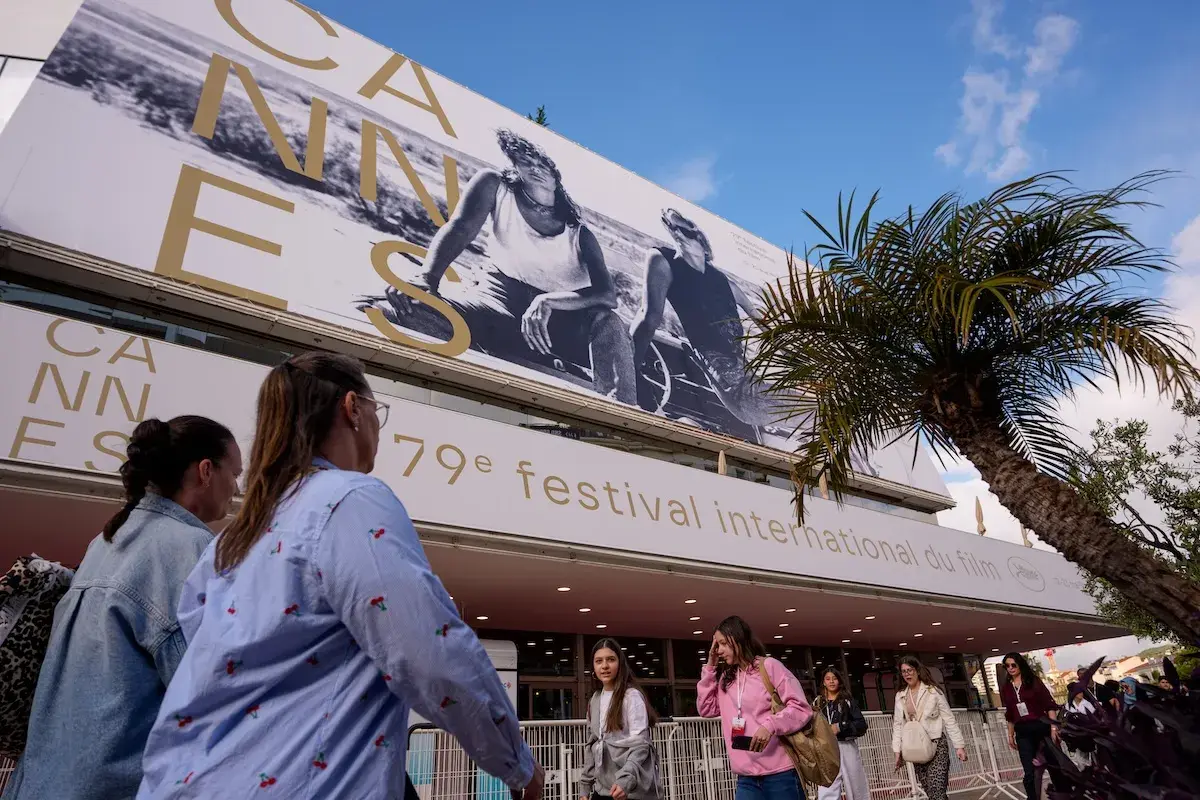 Persone camminano sotto il cartellone del Festival di Cannes, un evento che celebra il cinema internazionale, rivaleggiando con l'atmosfera di Hollywood.