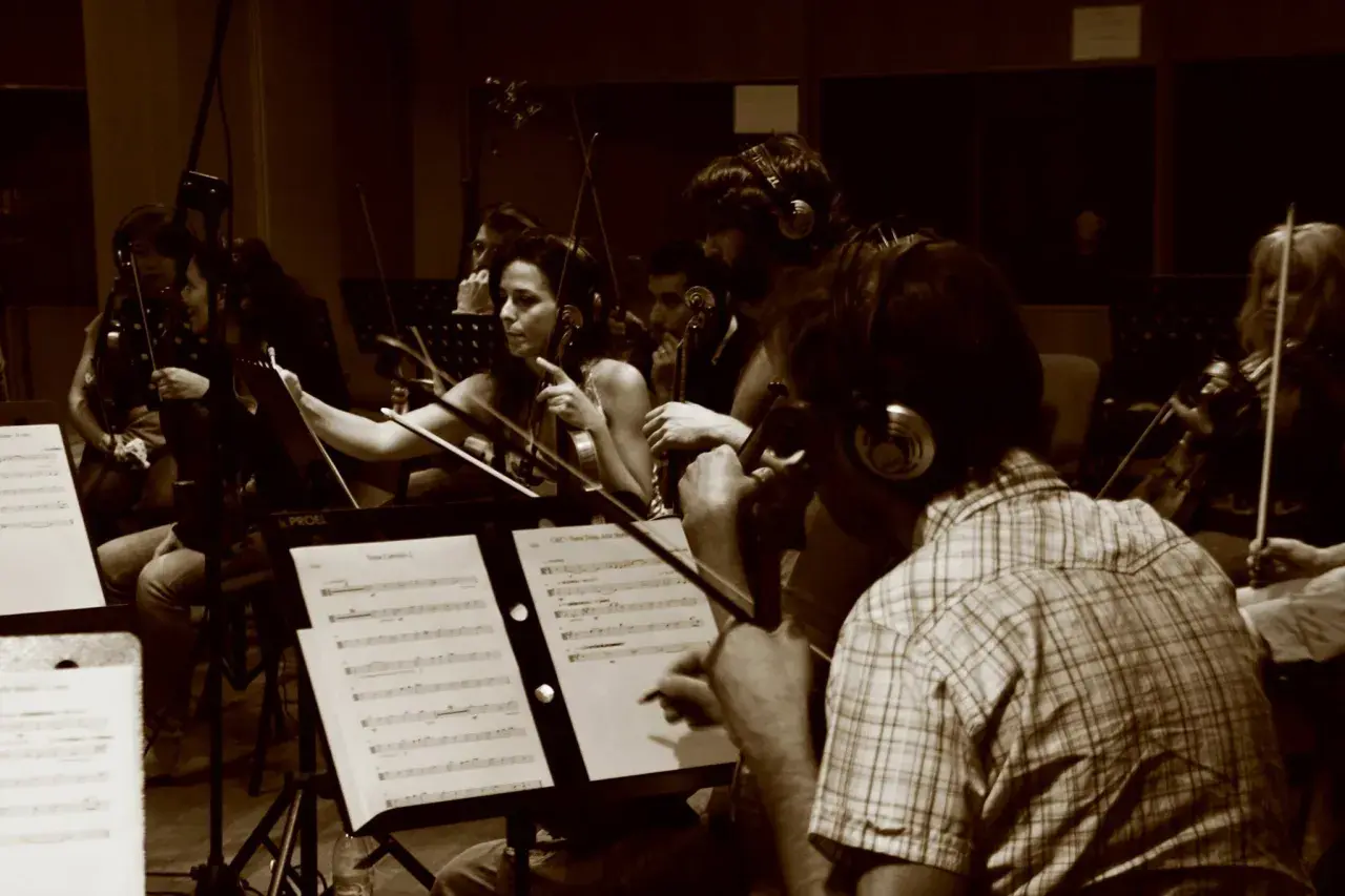 Orchestra di archi registra colonne sonore film italiani. Musicisti concentrati sugli spartiti, con cuffie per il monitoraggio.