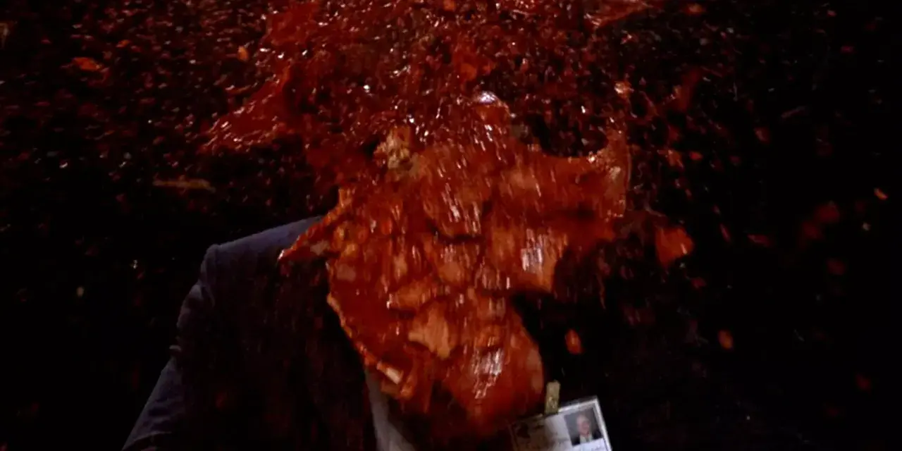 Un uomo in giacca e cravatta, vittima di un evento cruento, con sangue e detriti che esplodono in un'immagine tipica di un genere cinematografico con scene truculente.