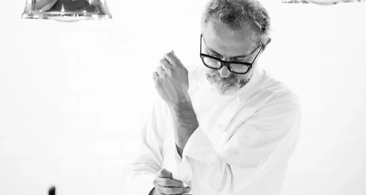 Julian works, aggiustandosi il polsino della giacca da chef. La sua espressione concentrata suggerisce la dedizione al suo mestiere.