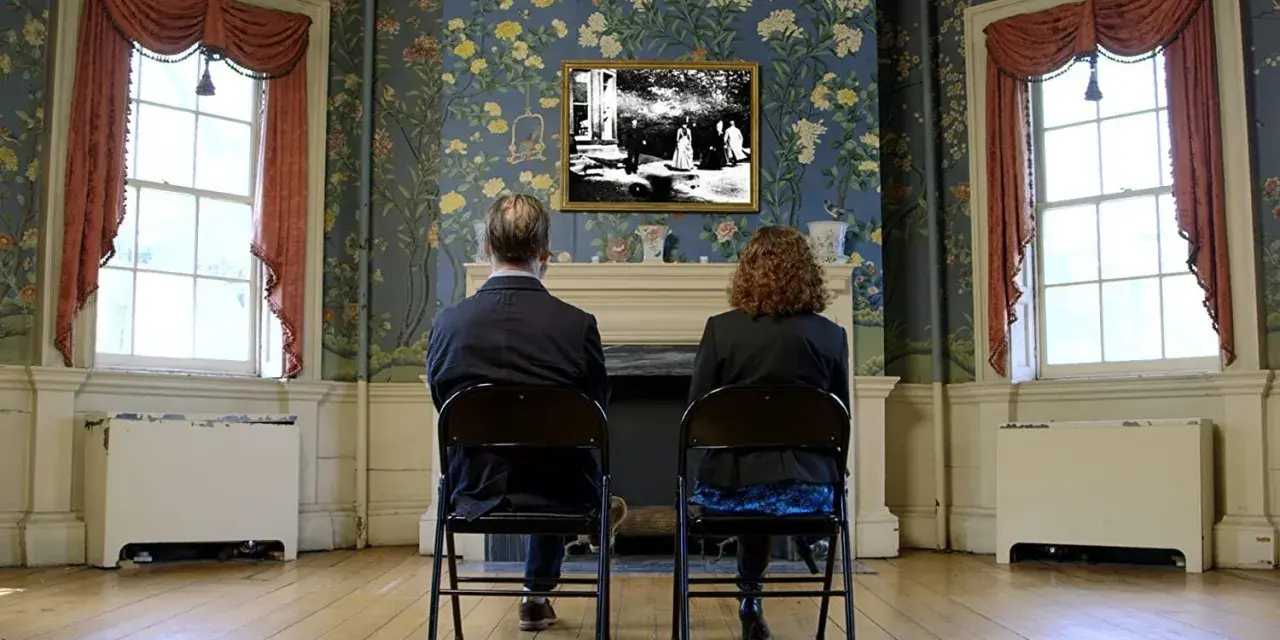 Coppia seduta di spalle, guarda un quadro con una scena di giardino, "Roundhay Garden Scene", su una parete fiorita.