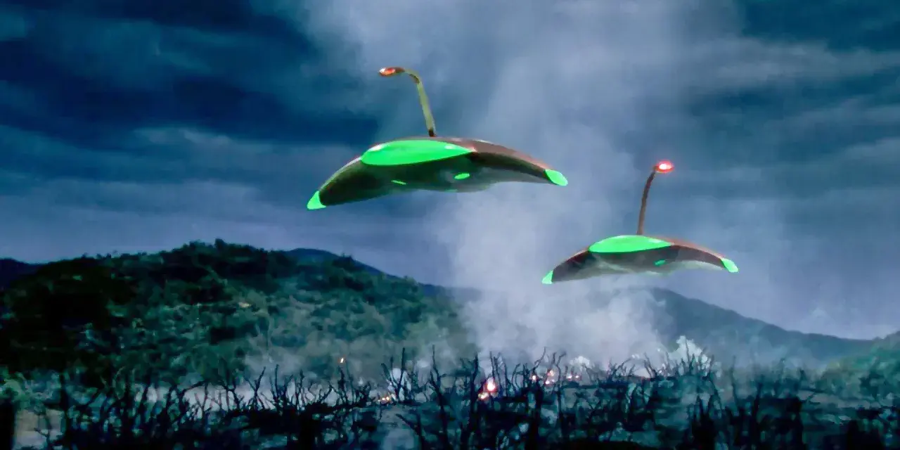 Due astronavi aliene sorvolano un paesaggio devastato, con fumo e fiamme che si levano dal terreno. La scena evoca la minaccia de "la guerra dei mondi (film 1953)".