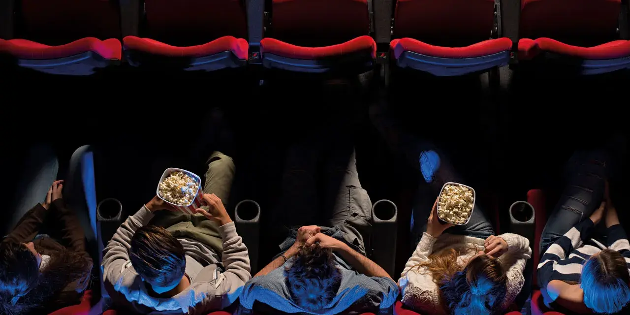 Persone sedute in un cinema, gustando popcorn, pronte per un film di Hollywood.