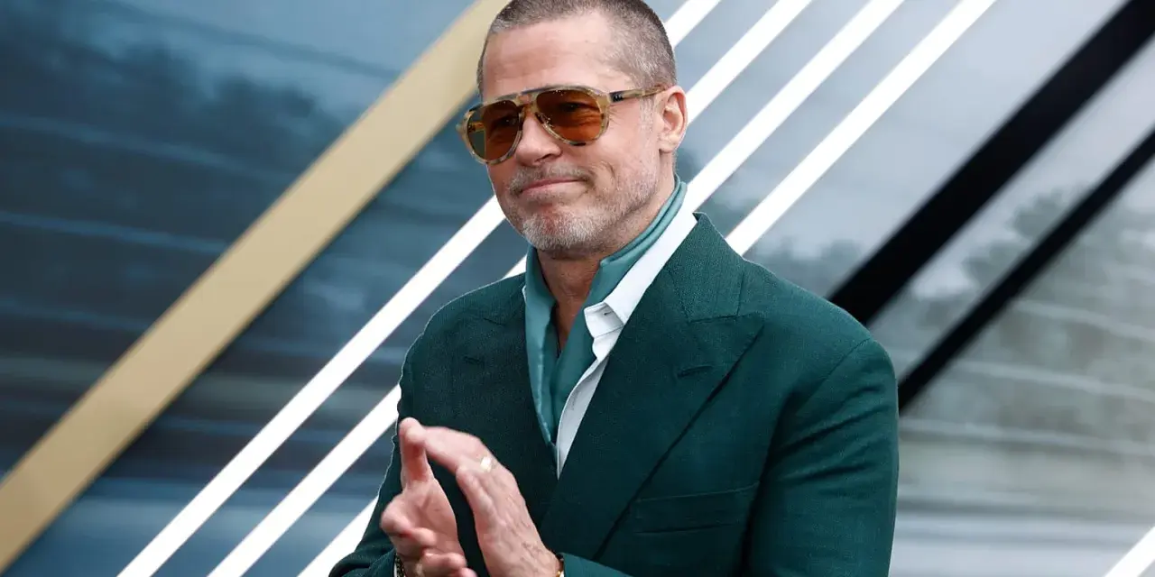 Brad Pitt, icona del cinema hollywoodiano, con occhiali da sole e completo verde, applaude con un sorriso.
