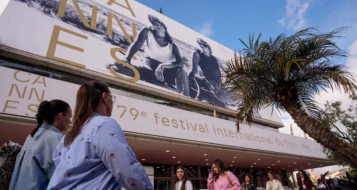 Persone camminano sotto il cartellone del Festival di Cannes, un evento che celebra il cinema internazionale, rivaleggiando con l'atmosfera di Hollywood.