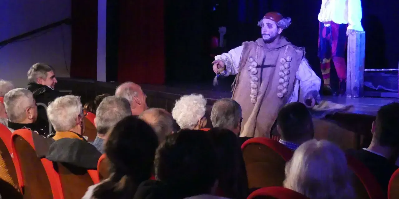 Attori sul palco, uno con un costume particolare, sembrano rompere la **quarta parete significato** parlando al pubblico.
