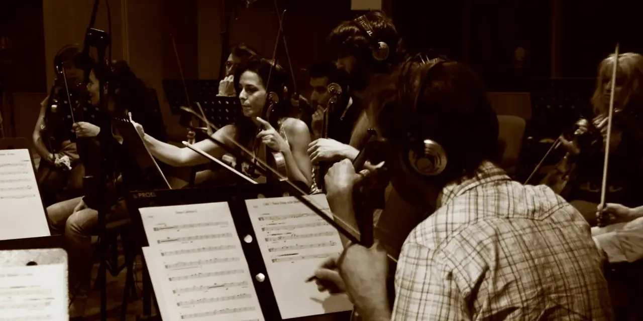 Orchestra di archi registra colonne sonore film italiani. Musicisti concentrati sugli spartiti, con cuffie per il monitoraggio.
