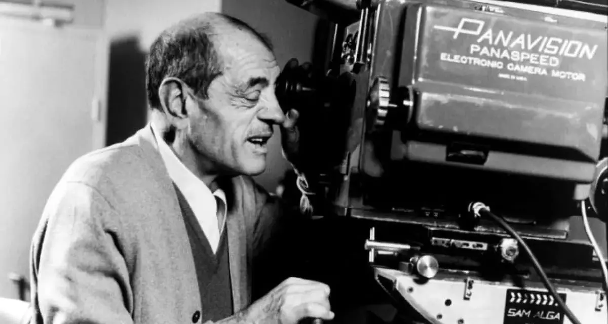 Un regista spagnolo, con un maglione grigio, guarda attraverso l'obiettivo di una cinepresa Panavision.