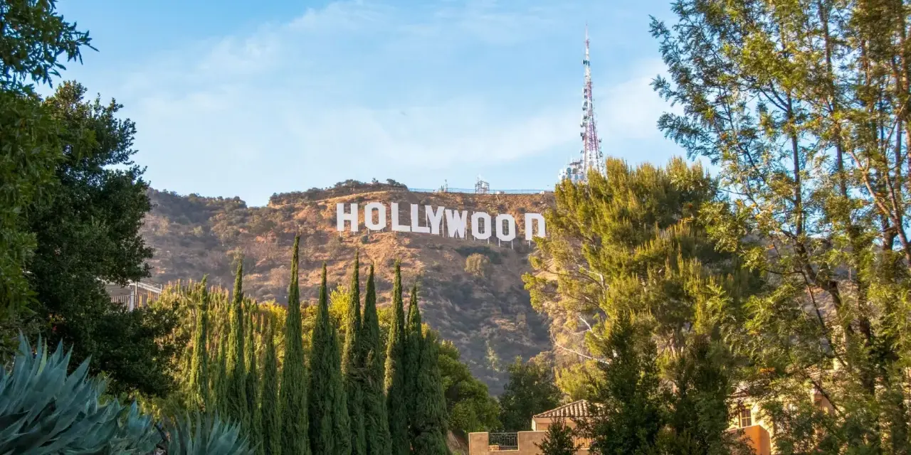 Il cartello "HOLLYWOOD" domina la collina, indicando dove si trova Hollywood, con alberi verdi e un cielo azzurro.