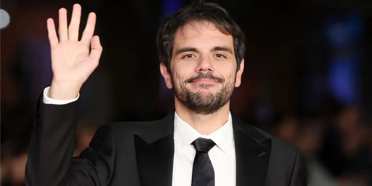 Valerio Vestoso saluta con la mano, sorridendo con un abito elegante.