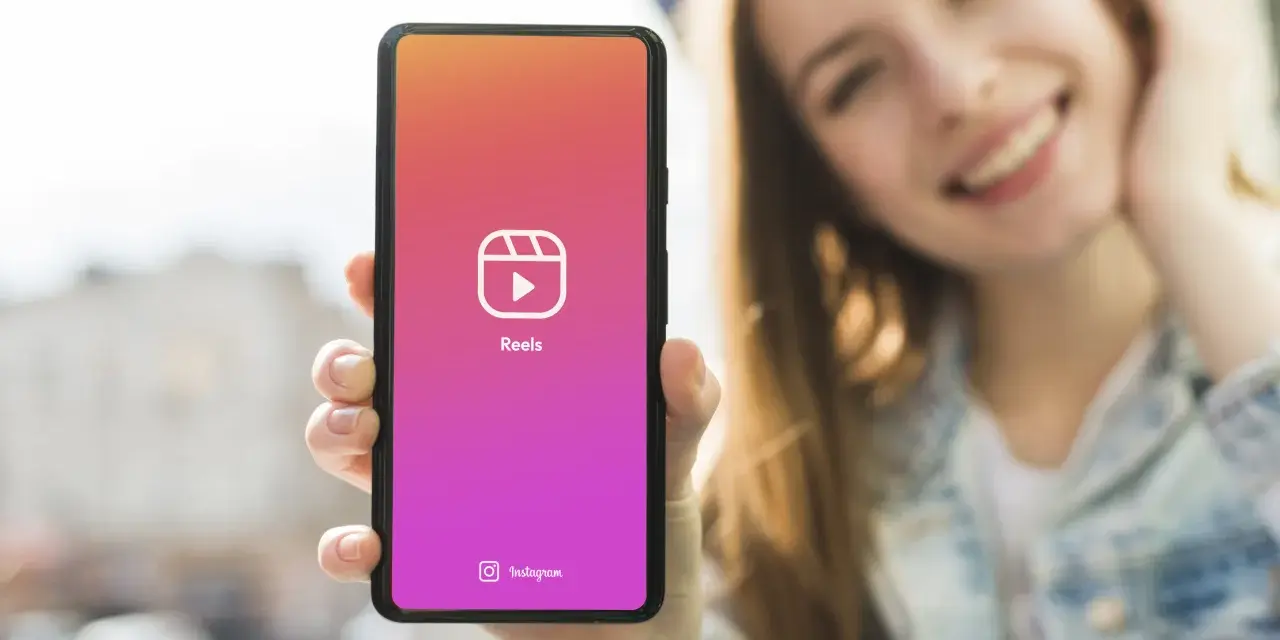 Una ragazza sorride mentre mostra il suo smartphone con l'icona di Reels, perfetta app per montare video e creare contenuti.