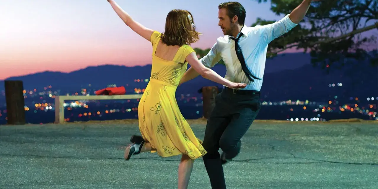 Coppia balla al tramonto, immersa nella musica diegetica che accompagna la loro danza, con la città illuminata sullo sfondo.
