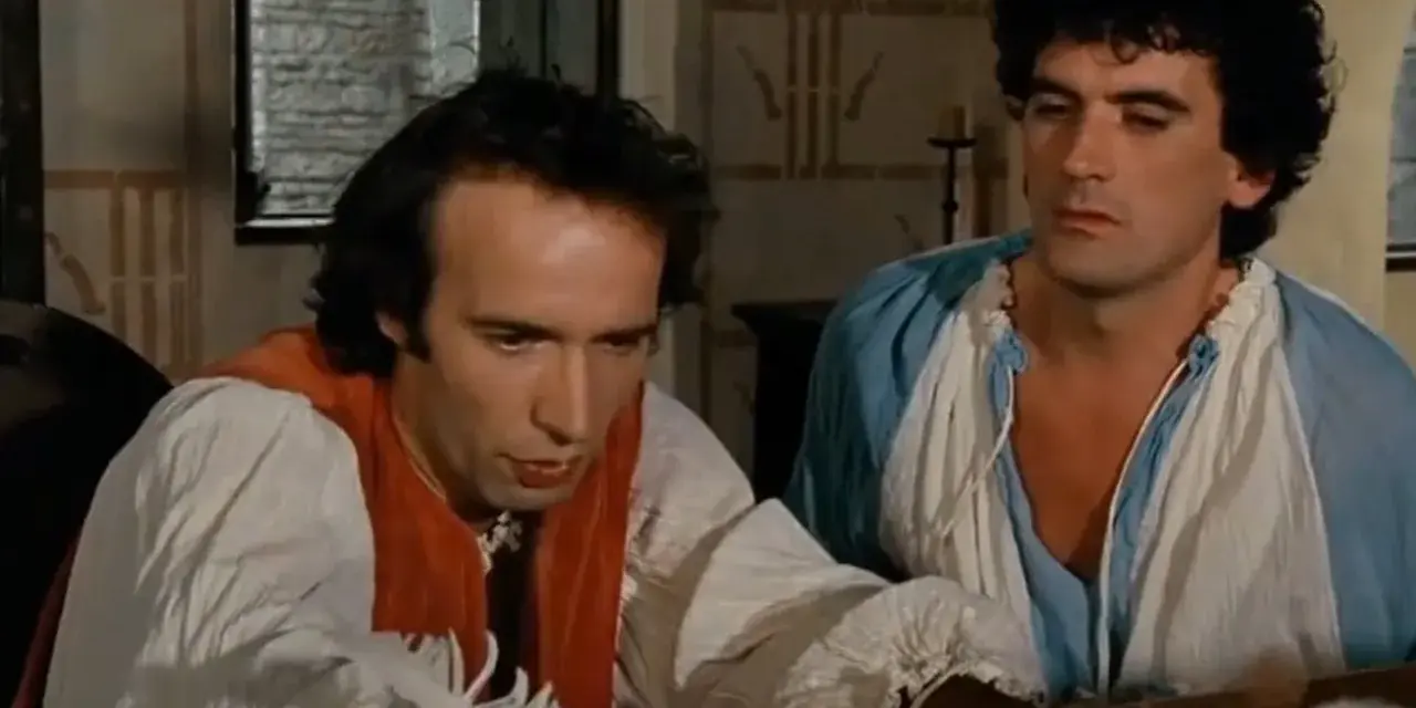 Due uomini in abiti d'epoca, uno scrive con una penna d'oca, in una scena che promette un film comico.