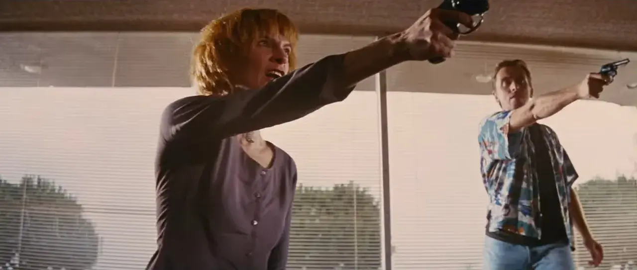 Donna e uomo puntano pistole, in una scena che ricorda un cliffhanger traduzione.