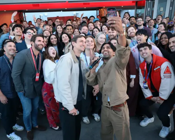 Un gruppo di persone sorride e fa un selfie a Hollywood, America. Alcuni tengono microfoni, creando un'atmosfera di festa.