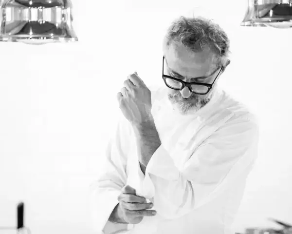 Julian works, aggiustandosi il polsino della giacca da chef. La sua espressione concentrata suggerisce la dedizione al suo mestiere.