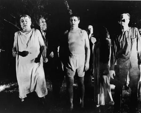 Un gruppo di persone dall'aspetto spettrale, un'immagine che evoca il significato di un b movie, cammina in un bosco di notte.