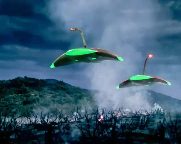 Due astronavi aliene sorvolano un paesaggio devastato, con fumo e fiamme che si levano dal terreno. La scena evoca la minaccia de "la guerra dei mondi (film 1953)".