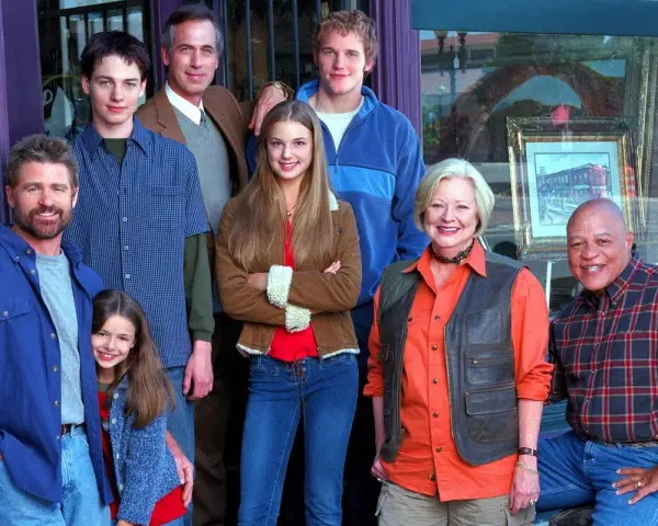 Cast di famiglie serie tv americane anni 2000, sorridono davanti a un negozio.