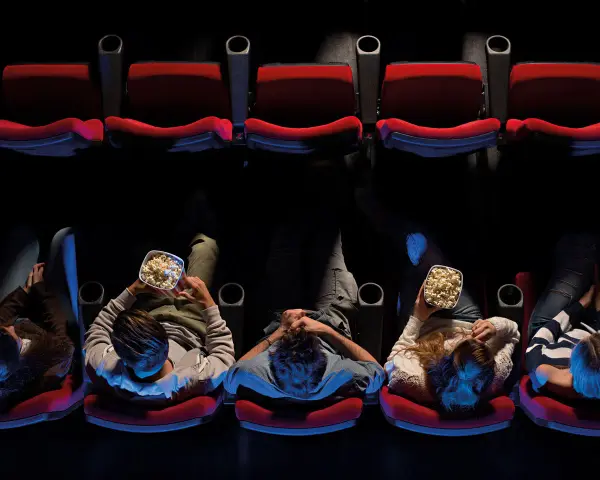 Persone sedute in un cinema, gustando popcorn, pronte per un film di Hollywood.