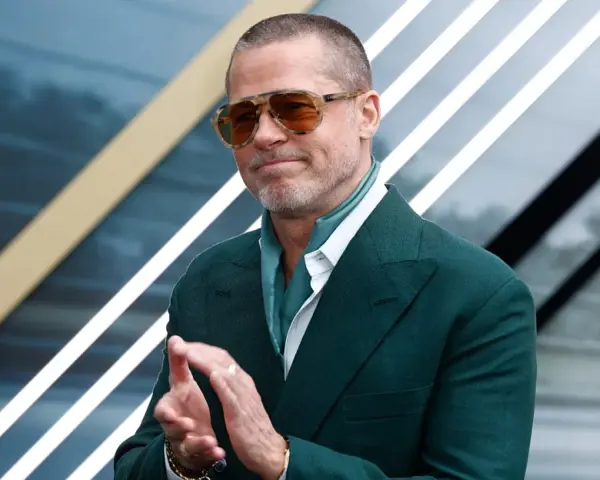 Brad Pitt, icona del cinema hollywoodiano, con occhiali da sole e completo verde, applaude con un sorriso.