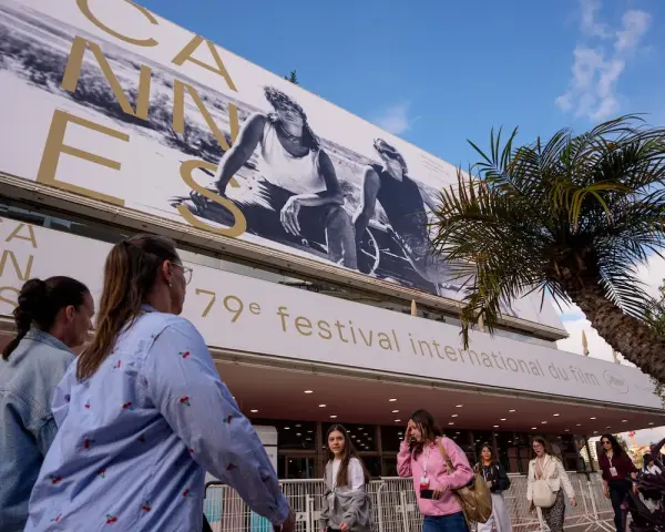 Persone camminano sotto il cartellone del Festival di Cannes, un evento che celebra il cinema internazionale, rivaleggiando con l'atmosfera di Hollywood.