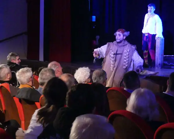Attori sul palco, uno con un costume particolare, sembrano rompere la **quarta parete significato** parlando al pubblico.
