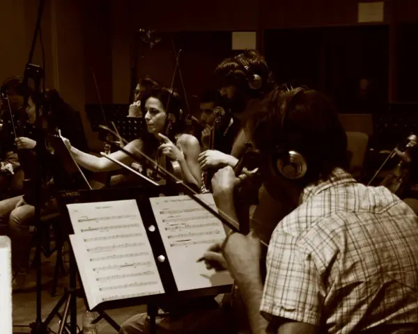 Orchestra di archi registra colonne sonore film italiani. Musicisti concentrati sugli spartiti, con cuffie per il monitoraggio.