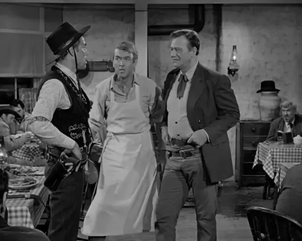 Inquadratura americana di tre uomini in un saloon. Uno indossa un grembiule, gli altri abiti western.