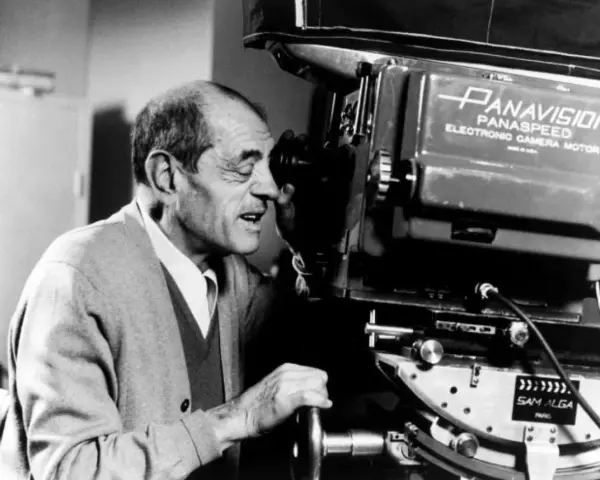Un regista spagnolo, con un maglione grigio, guarda attraverso l'obiettivo di una cinepresa Panavision.